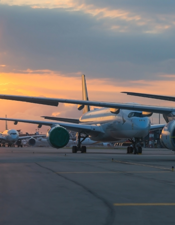 Airplanes on tarmac at sunset, airport scene. Commercial jets, including a Cathay Pacific plane, are parked. Airport fencing not visible.