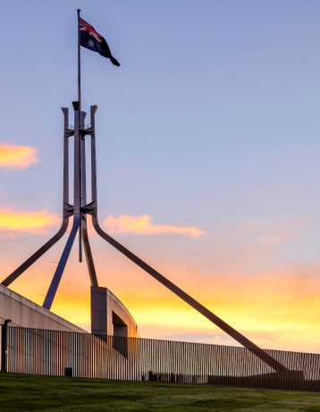Australian Parliament House with flag and temporary government fencing at sunset. Canberra architecture and sky.