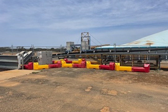 Gallery image: Red and yellow barriers line an industrial site. Conveyor belts and a metal structure are visible against a partly cloudy sky.