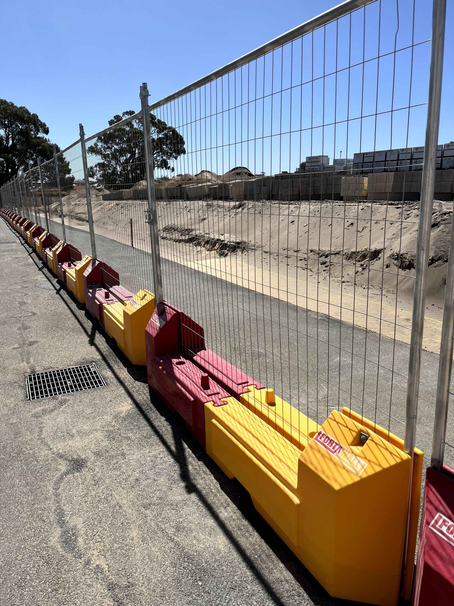 Gallery image: Temporary fencing with red and yellow water filled barriers. A construction site is visible behind the fence.