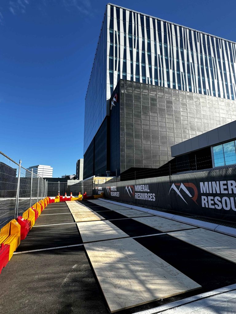 Gallery: Mineral Resources site with black and white checkered ground cover, fencing, and a modern office building under a clear blue sky.