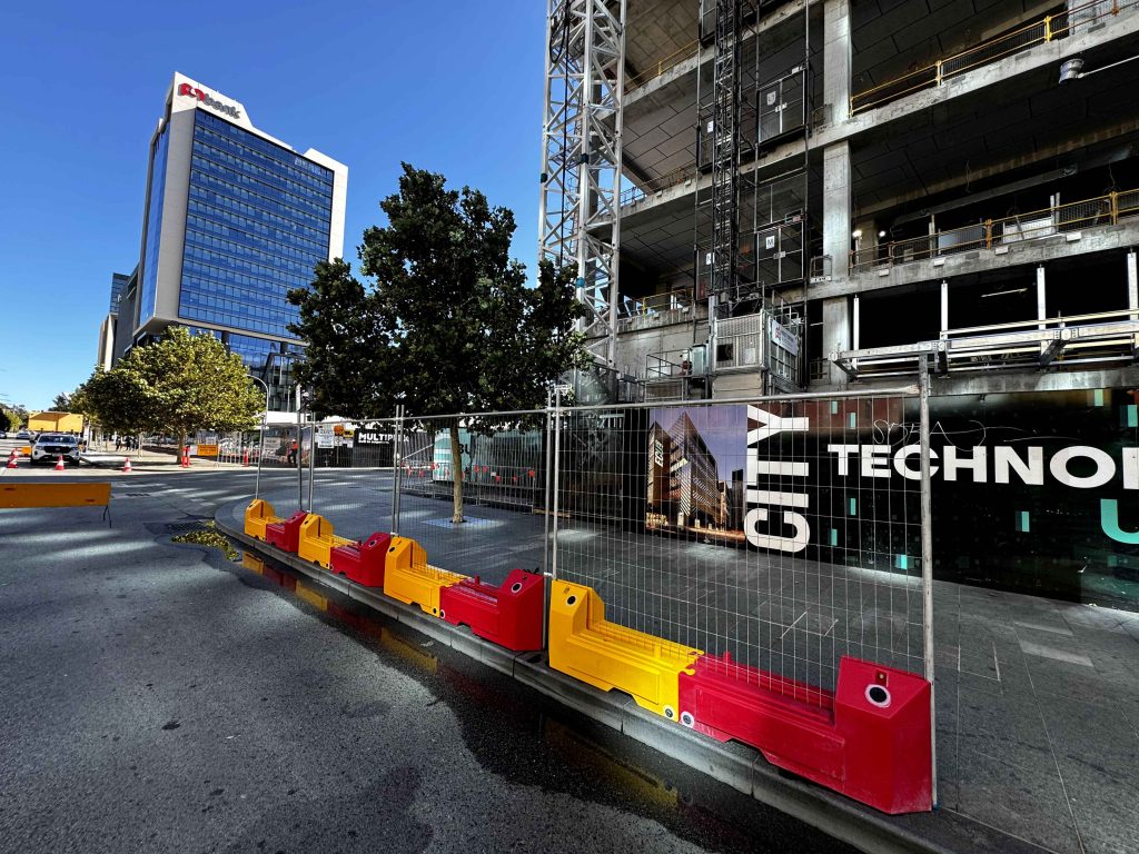Gallery: City construction site with red and yellow barriers. Building under construction with scaffolding. Modern office building in the background.