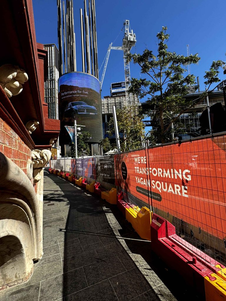 Gallery: Yagan Square transformation with construction fencing. A large digital billboard displays a car ad. A crane is visible in the background.