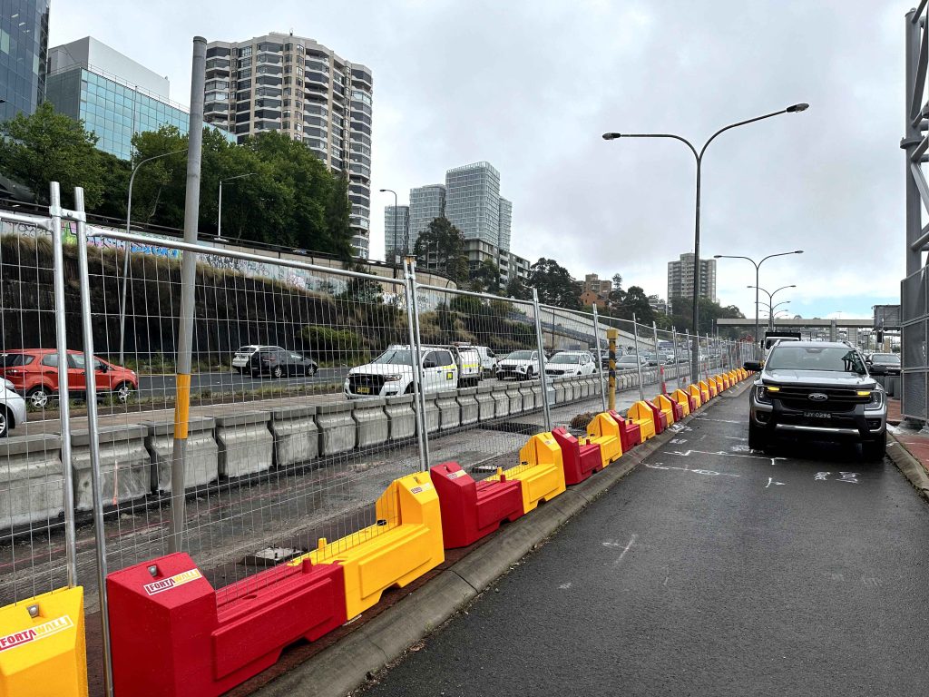 Gallery: Urban highway scene with traffic. Red and yellow barriers line the road, with city buildings in the background. Cars are visible on the highway.