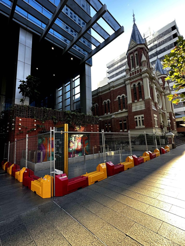 Gallery: Modern building contrasts with a historic church. A red and yellow barrier fences off a colorful mural. Urban architecture and art.